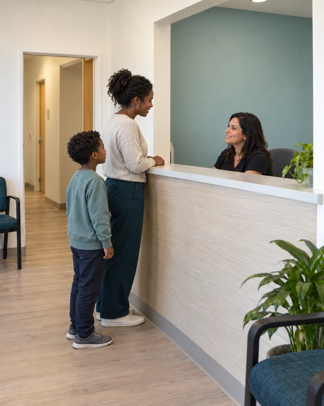 A parent and son speaking with a receptionist at a therapy clinic front desk.